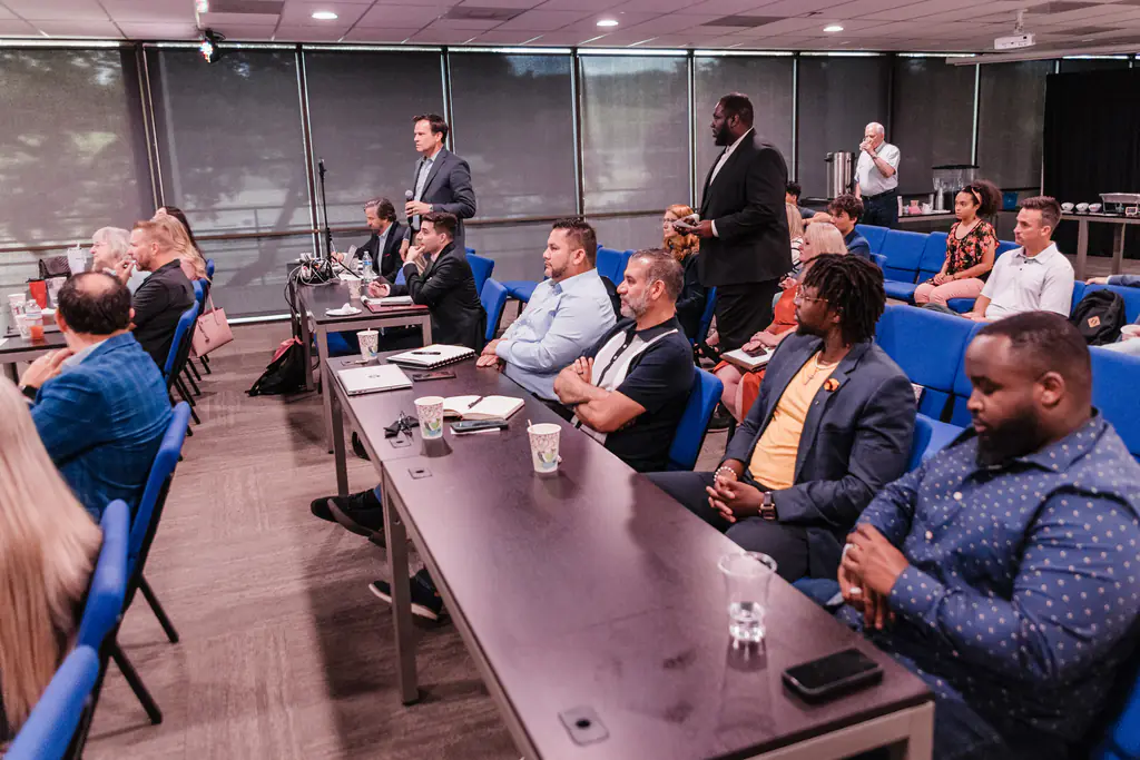 Attendees seated at tables listening to speakers at the Kinected Symposium