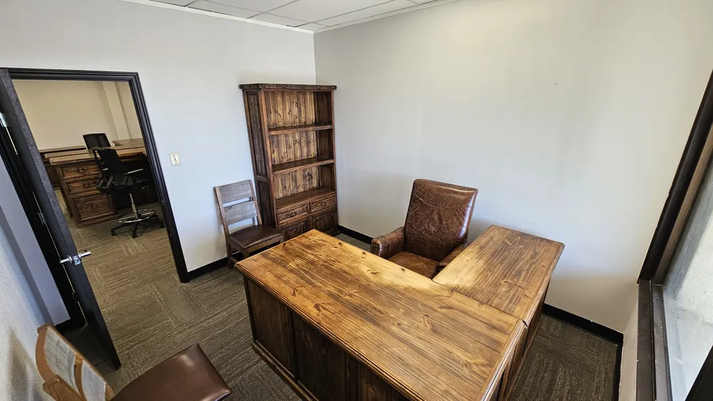 Private office in Suite 211 with an L-shaped desk, bookcase, and door to the team area