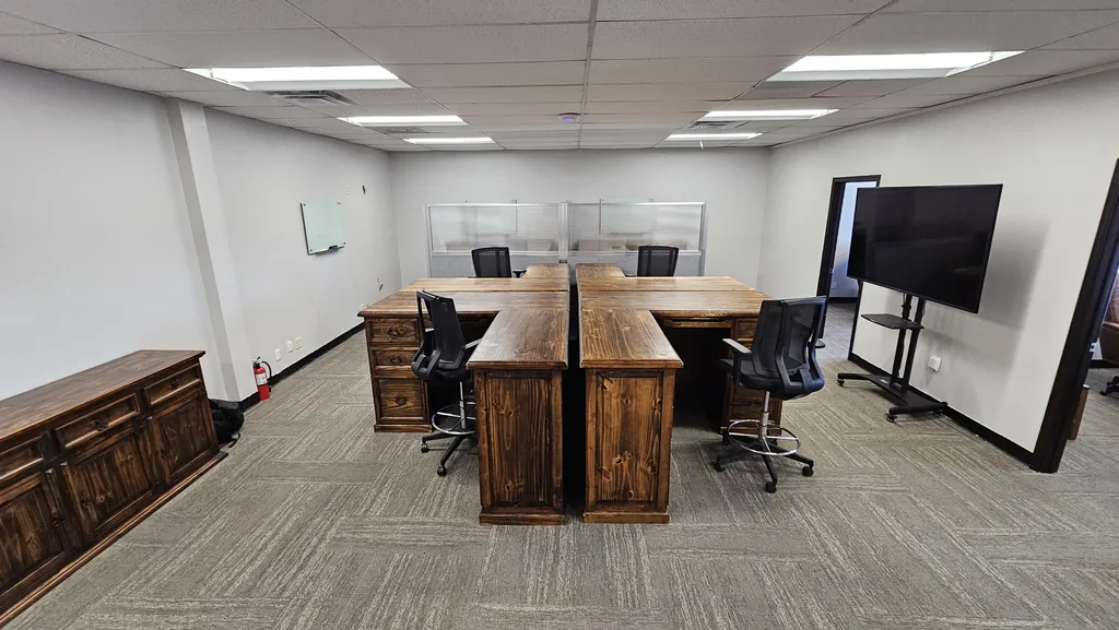 Four-desk team pod, glass whiteboard, and mobile display screen inside Suite 211